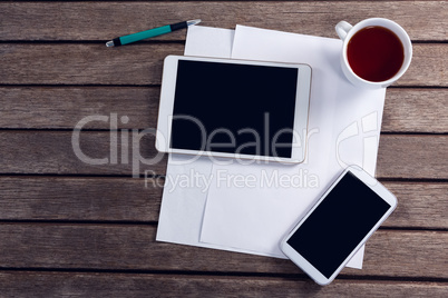 Digital tablet, mobile phone, black coffee and blank paper on wooden table
