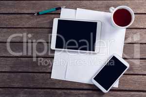 Digital tablet, mobile phone, black coffee and blank paper on wooden table