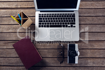 Laptop, diary, spectacles, camera and pen holder on wooden table