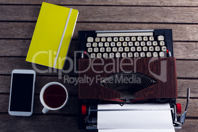 Vintage typewriter, diary, black coffee and smart phone on wooden table