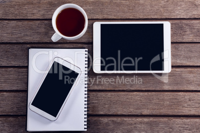 Digital tablet, mobile phone, black coffee and diary on wooden table