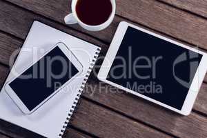 Digital tablet, mobile phone, black coffee and diary on wooden table