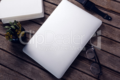 Laptop, diary, pot plant, spectacles and smart watch on wooden table