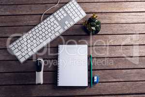 Keyboard, diary, pot plant, stationery and stapler on wooden table