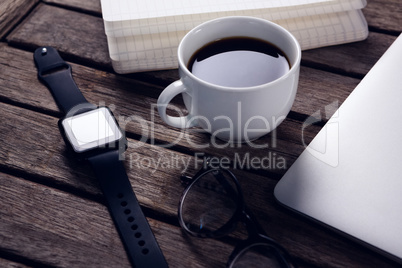 Black coffee with organizer, laptop, spectacles and smart watch on wooden table
