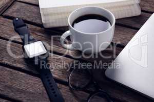 Black coffee with organizer, laptop, spectacles and smart watch on wooden table