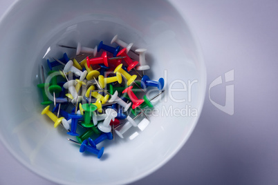 Colorful push pins in bowl on white background