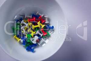 Colorful push pins in bowl on white background