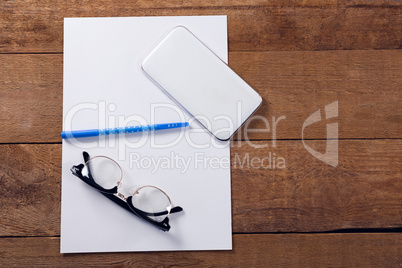 Blank paper, mobile phone, pen and spectacles on wooden table