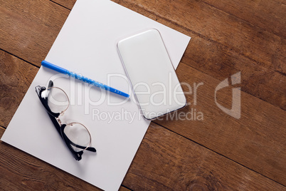 Blank paper, mobile phone, pen and spectacles on wooden table