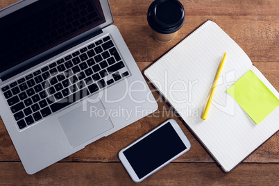 Laptop, mobile phone, disposable glass, pen and organizer on wooden table