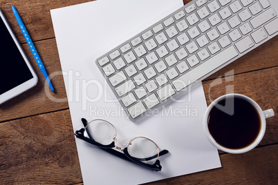 Black coffee, keyboard, spectacles and paper on wooden table
