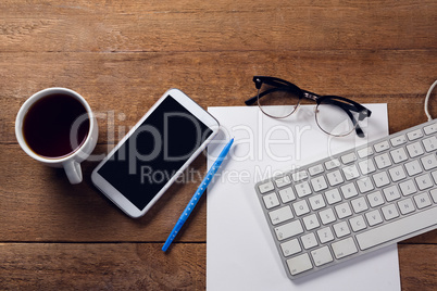 Mobile phone, keyboard, paper, spectacles, pen and coffee on wooden table