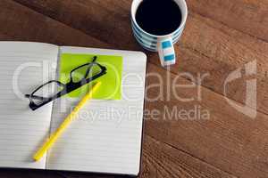 Black coffee with organizer, spectacles, pen and sticky note on wooden table