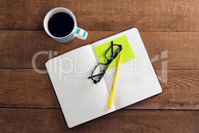 Black coffee with organizer, spectacles, pen and sticky note on wooden table