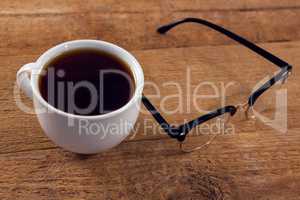 Black coffee and spectacles on wooden table