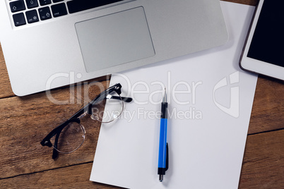 Digital tablet, laptop, paper, pen and spectacles on wooden table