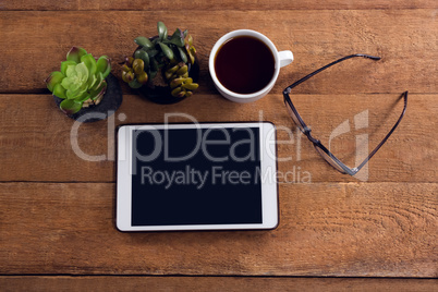 Pot plant, black coffee, spectacles and digital tablet on wooden table