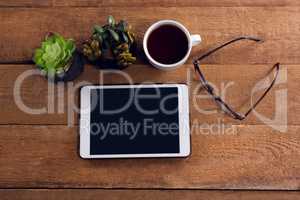 Pot plant, black coffee, spectacles and digital tablet on wooden table