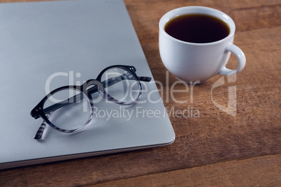 Spectacles on laptop with black coffee at desk