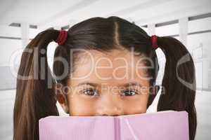 Composite image of schoolgirl covering mouth with book
