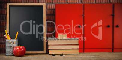 Composite image of books by slate with desk organizer and apple on wooden table