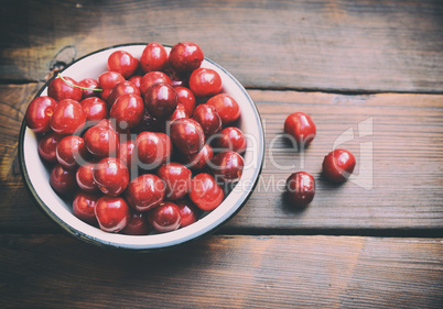 Ripe red cherry in an iron plate on a brown table