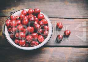 Ripe red cherry in an iron plate on a brown table