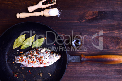 Carp in spices on a black cast-iron frying pan