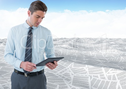 Businessman using tablet in sea of documents under sky clouds