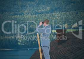 Businessman on ladder with binoculars over roof and forest