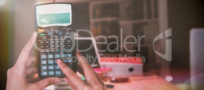 Composite image of cropped hands of businesswoman using calculator