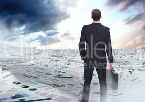 Businessman holding briefcase in sea of documents under sky clouds opening