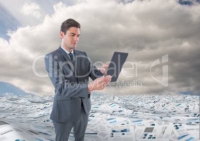 Businessman on tablet in sea of documents under sky clouds