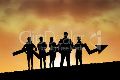 Business people holding an arrow silhouette against sunset or sunrise