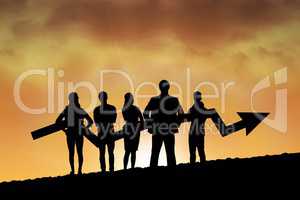 Business people holding an arrow silhouette against sunset or sunrise