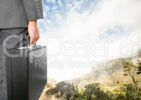 Businessman holding briefcase under sky clouds and mountain landscape