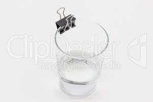 A glass with a little water in it and a binder clip on it's rim.