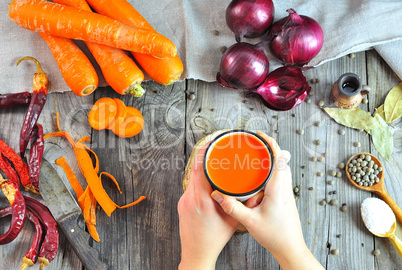 Female hands holding carrot juice in an iron mug