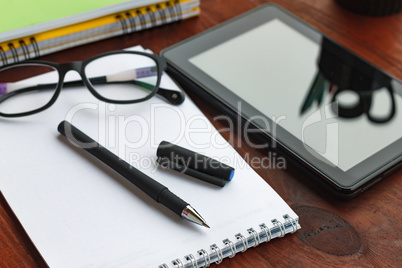 The concept: the beginning of work. Pen, open notebook, tablet computer and glasses on office desk.