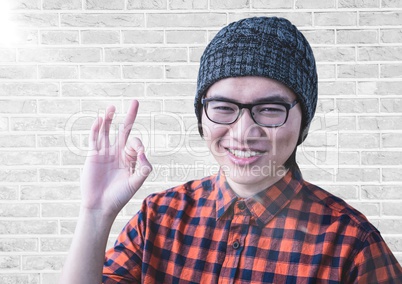 Close up of millennial man making ok sign with flare against white brick wall