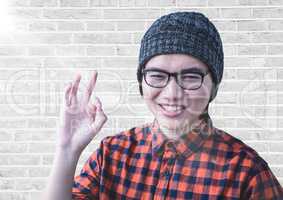 Close up of millennial man making ok sign with flare against white brick wall