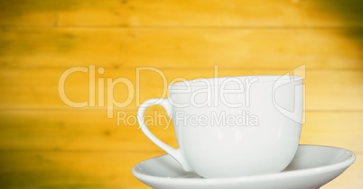 White cup and saucer against blurry yellow wood panel
