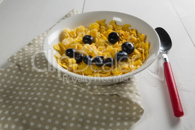 Wheaties cereal and blueberry in bowl with table cloth and spoon