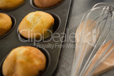 Close up of muffins in tin by wooden spoon and wire whisk