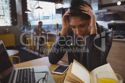 Frustrated woman with book and laptop in cafe