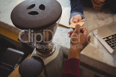 Cropped hand of owner receiving payment from customer by grinder in cafe