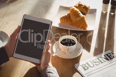 Cropped hands of businessman with breakfast using tablet in cafe