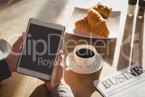 Cropped hands of businessman with breakfast using tablet in cafe