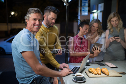 Friends using electronic gadgets while having coffee